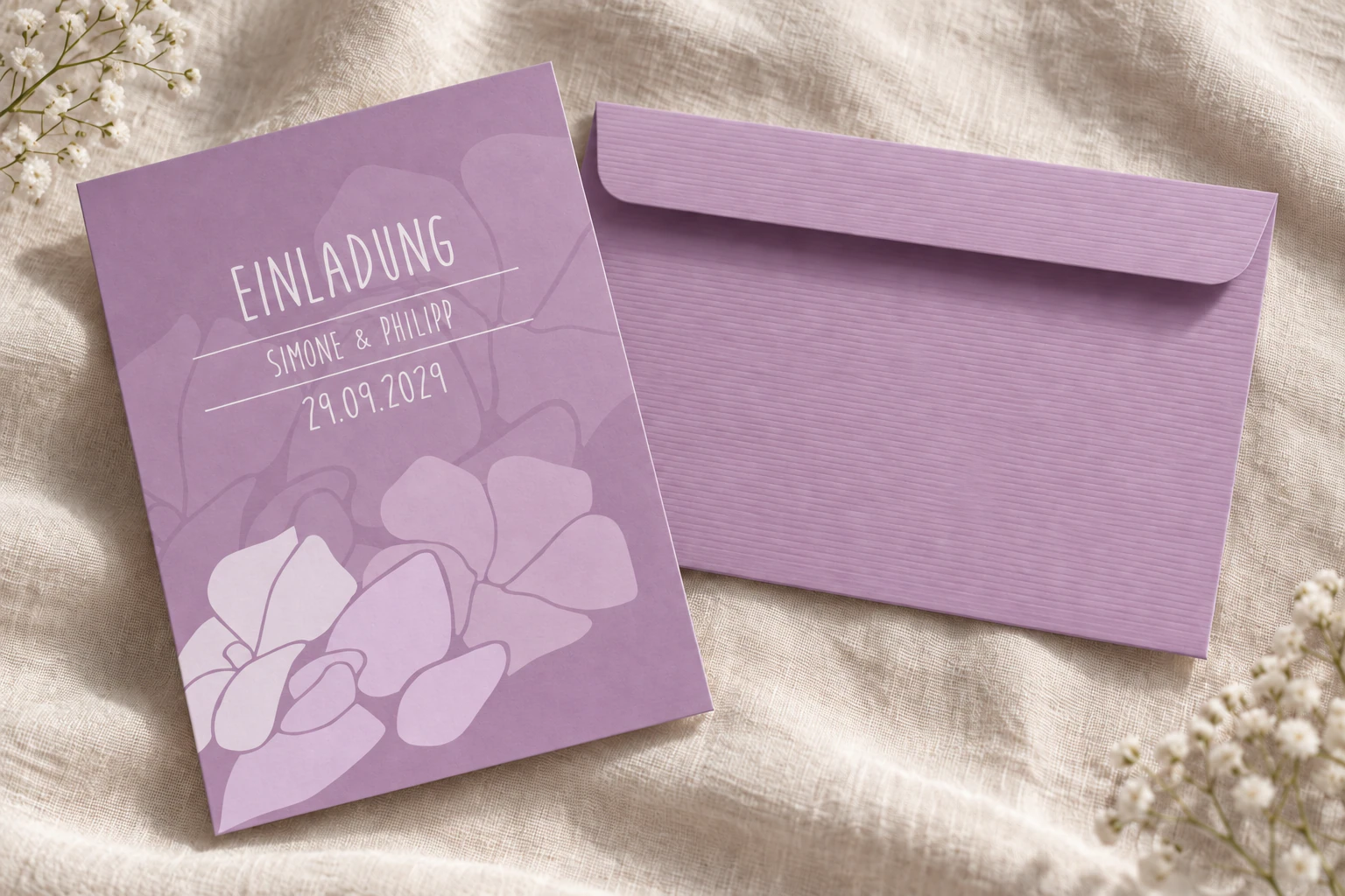 Fliederfarbenes geripptes Kuvert neben der violetten Magnolien-Hochzeitseinladung mit hellen Blüten und weißer Schrift